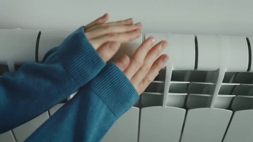 Women's Hands Touch the Heating Radiator in the Apartment