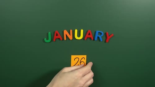 Hand sticking a sticker 26 January calendar day on school board. 26 date of January. Twenty sixth