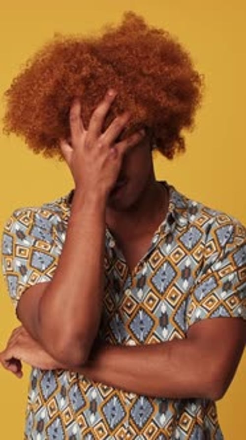 Bored guy is annoyed, covers his face with his palm isolated on yellow background in studio
