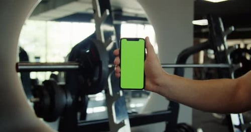 Male Hand Holding a Smartphone with Empty Green Screen Chromakey at the Gym