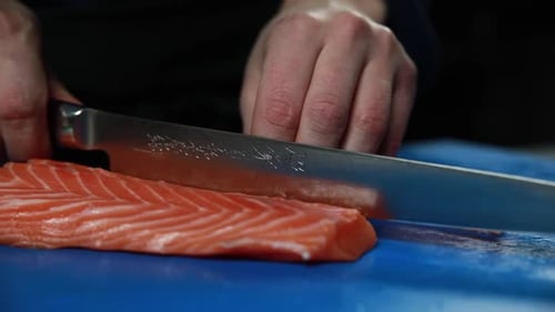 The chef slices a piece of raw salmon