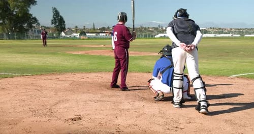 Playing baseball, batter in maroon uniform preparing to hit pitch on field