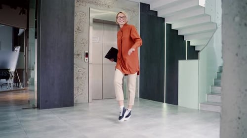 Happy joyful young and attractive woman dancing victory dance in corridor or hall of modern business