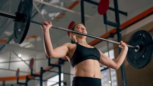 in the Gym Coach Girl in a Black Top is Standing Doing Exercises with a Barbell and Weights