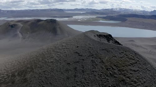 Aerial across edge of volcanic crater towards lake in Highlands Iceland.
