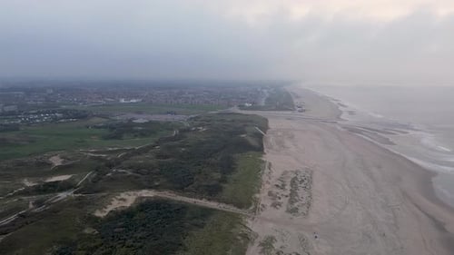 Aerial view of a serene coastline featuring a sandy beach, gentle ocean waves, and lush greenery.