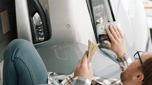 Funny. Happy young man applying money wiping the headlights of the car by american dollar