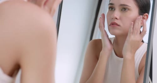 Woman Examines Face in Mirror Indoors