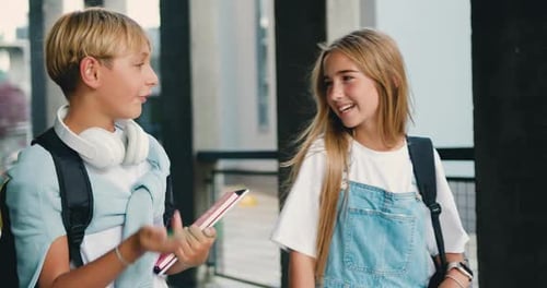 School couple. Friendly children with backpacks walking on stairs near school after lessons. Talking