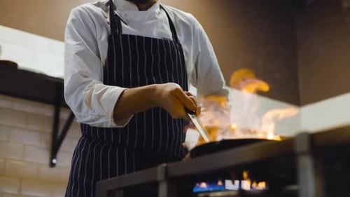 Zeitlupen-Track nach rechts und dann nach oben, wie der Koch in einer professionellen Küche mit Feuer in der Pfanne kocht