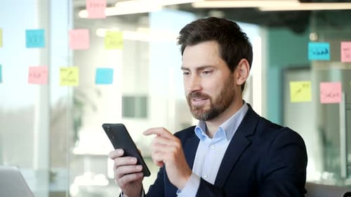 Confident businessman in suit using phone in contemporary office. Smiling male enjoying work