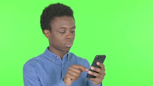 Young African Man with Loss on Smartphone on Green Background