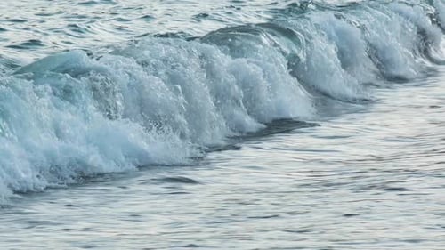 Slow motion of beautiful blue sea water waves splashing against tropical sand beach. Pan shot.