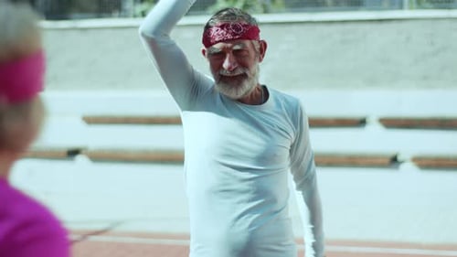 Senior man warms up on running track with friend