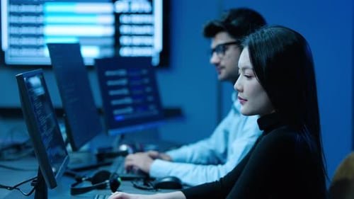 Smiling young female IT developer looking at camera while working on computer with male colleague