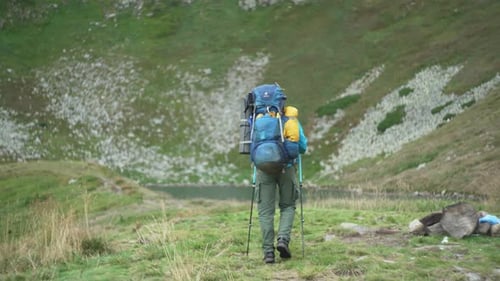 A tourist with a large backpack approaches a mountain lake and makes a stop