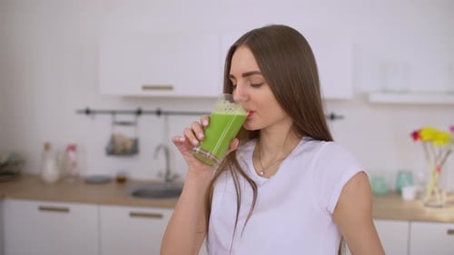 Woman Drinks Green Smoothie in Bright Kitchen