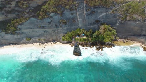 Aerial view of a remote tropical beach nestled against towering cliffs and surrounded by lush vegeta