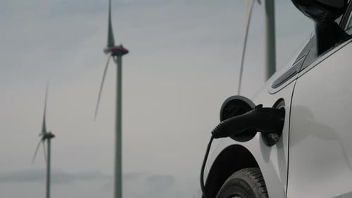 Electric Car Charging near Wind Turbines on Sunny Day