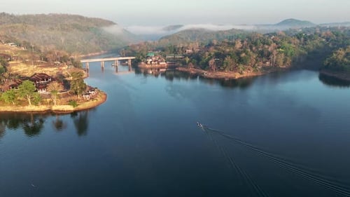 Drone avançando sobre o lago Khwae Noi, revelando a ponte Songkalia ao fundo, em Songklabur