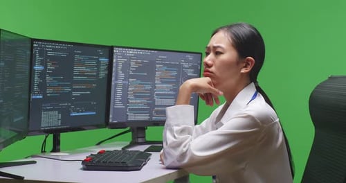 Asian Woman Developer Thinking While Write Code With Multiple Screens In Green Screen Studio