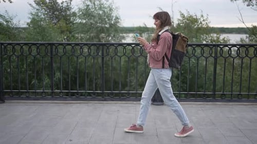 Young Woman Walks With Phone on City Path