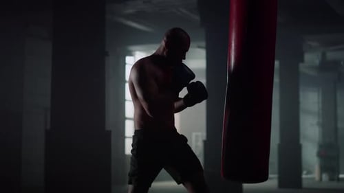 Muscular man silhouette boxing training with punching bag at dark gym cardio workout