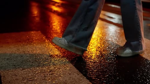 Detail of a Person's Feet in Wornout White Sneakers Stepping on a Wet Reflective Street at Night