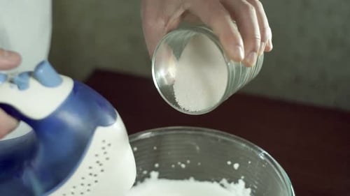 Sugar Pouring From Glass to Mixing Bowl. Closeup. Mixing Sweet Cream. Baking