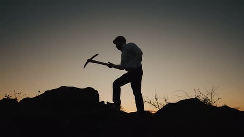 Silhouette eines Mannes mit Schutzhelm schlägt mit Spitzhacke auf Felsen, Krypto-Mining, Seitenansicht eines Geschäftsmannes in