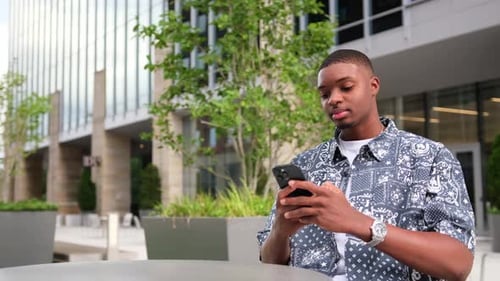 Young African American Man Focused on Smartphone in Vibrant Outdoor Urban Area