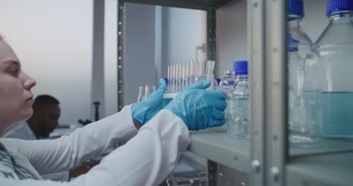 Medical Science Lab Female Chemist in White Coat Takes Test Tubes From the Shelf