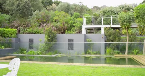 Camera is starting to pan to reveal pool, deck, table, shrubs and tree for garden tour