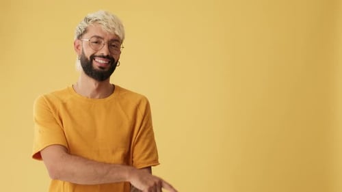 Smiling man pointing fingers to show advertising space, isolated on yellow background in studio