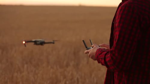 Farmer Holds Remote Controller with His Hands While Quadcopter is Flying on Background Drone Fliew