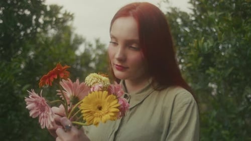 Woman Smelling Gerbera Daisies in Green Garden