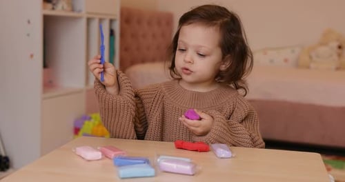 Young Girl Plays with Colorful Modeling Clay at Table