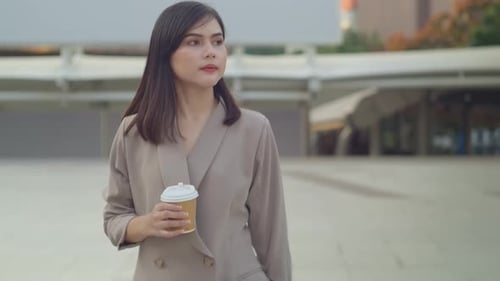 A young beautiful businesswoman is drinking coffee walking in Modern city