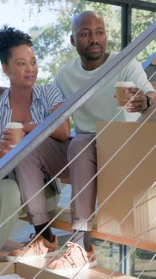 Vertical video: Placing cup on box, couple sitting on wooden stair pointing, planning room layout