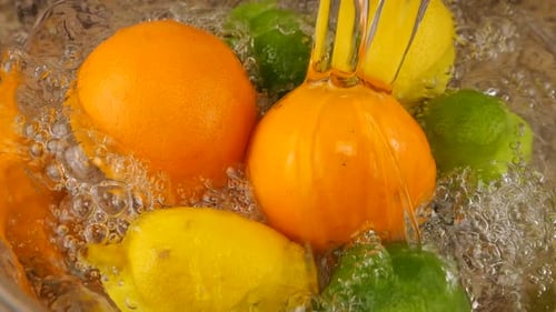 A jet of water falls on citrus fruits, orange, lemon and lime in a glass bowl. Slow motion.