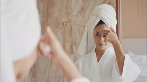 Woman in Robe Applying Facial Cream in Mirror