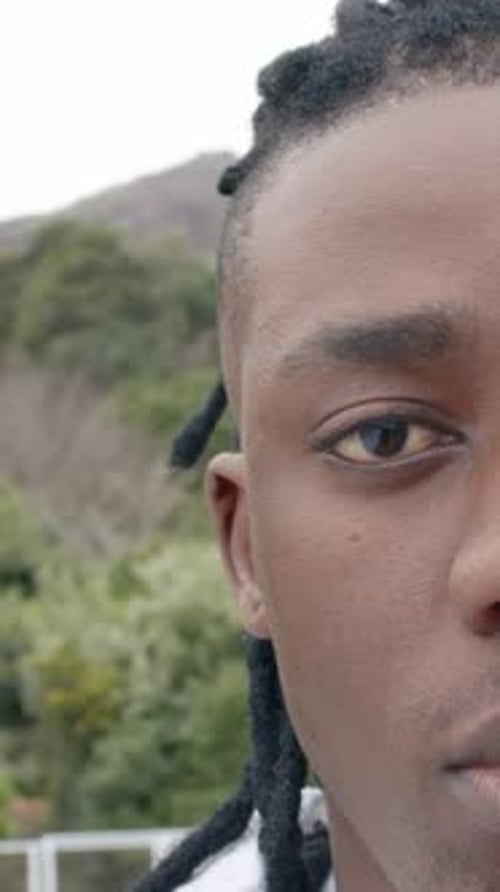 Vidéo verticale : Un homme souriant avec des serrures sur le dessus lumineux, clignotant après le regard, se déplaçant directement sur le pont, le rail