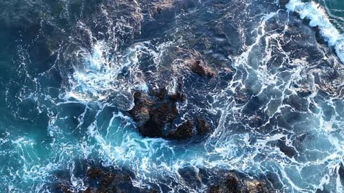 Waves Hit the Dark Rocks Top View Sea Water Splashes Over the Stones Sea Foam Covers Rocky Beach The