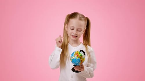 Glückliches Mädchen, das einen Globus hält und vor rosafarbenem Hintergrund lächelt, während es etwas über die Welt lernt