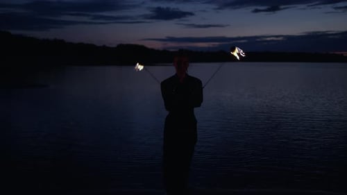 Performer Juggling Fire Balls on Dark Lakeside Beach