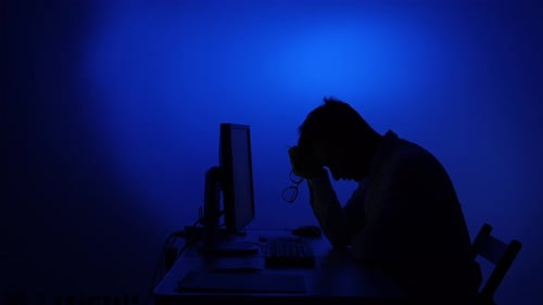 Silhouetted man at computer looks stressed and tired