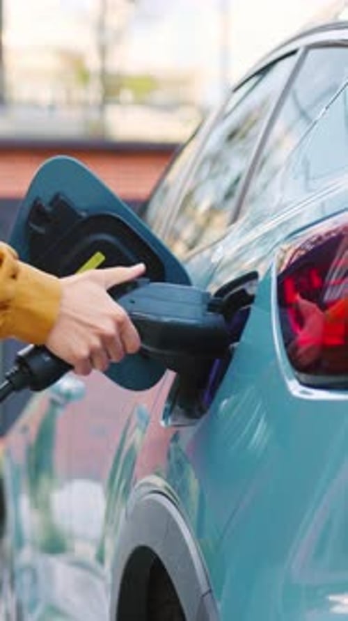 Nahaufnahme weiblicher Hände, die ein Elektroauto-Ladegerät an ihr Fahrzeug im Freien anschließen