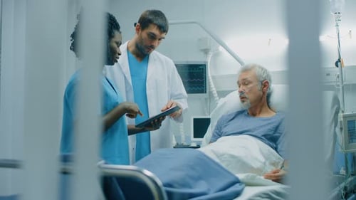 In the Hospital, Senior Man Lying in the Bed, Talks with Doctor and Nurse who Use Tablet Computer.