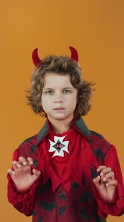 Young Boy in Devil Costume Growling and Clawing on Orange Background