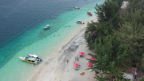 Aerial top down of tropical turquoise water and boats docked on white sand beach in Gili Islands